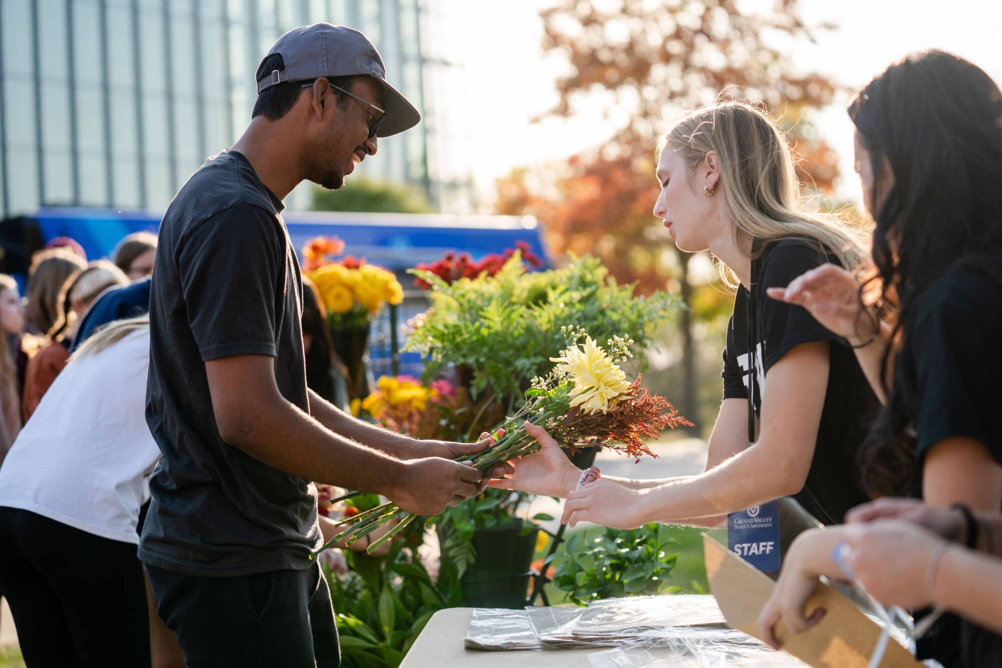 A woman sells flowers to a man on campus